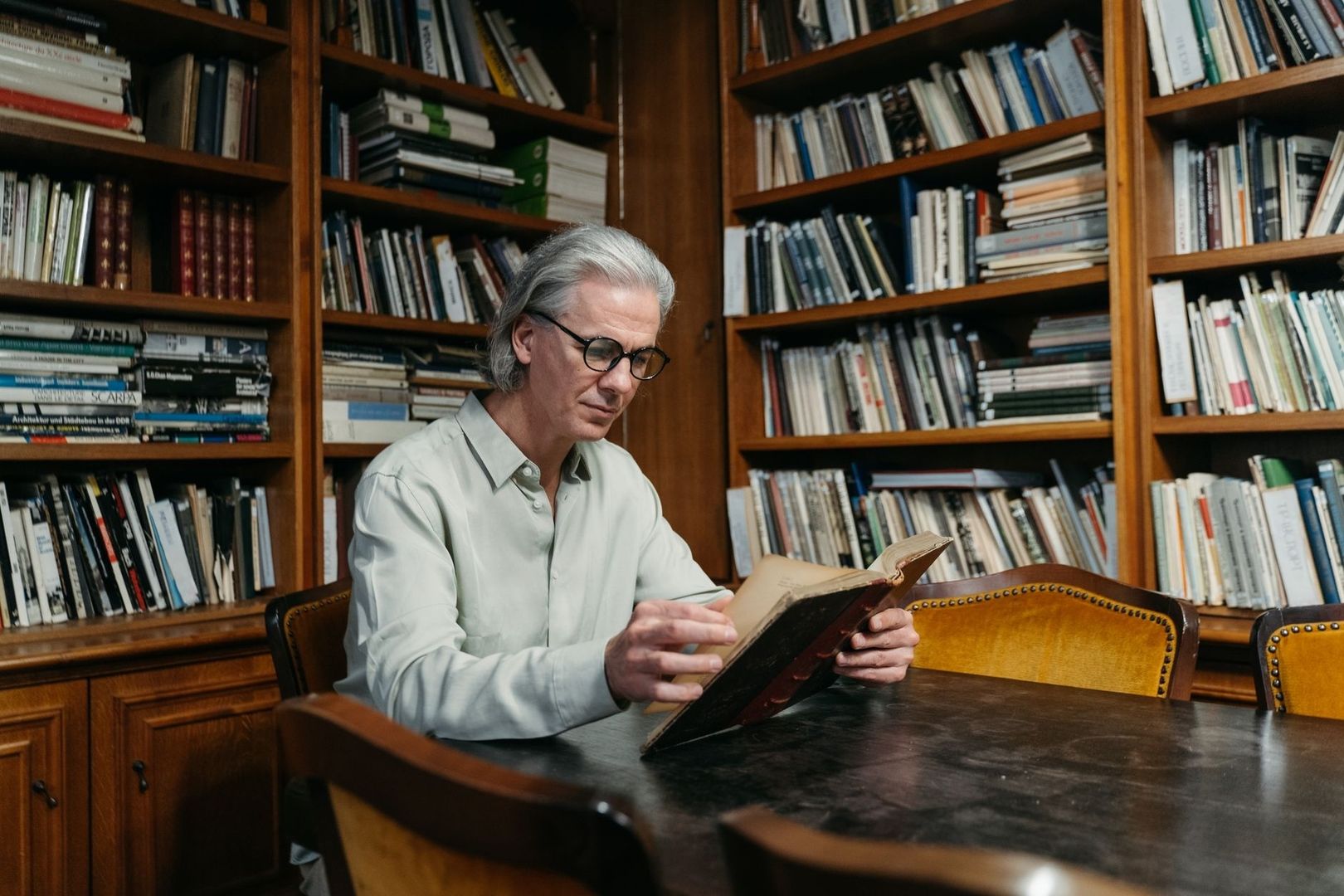 Man met bril leest een oud boek tussen hoge boekenkasten