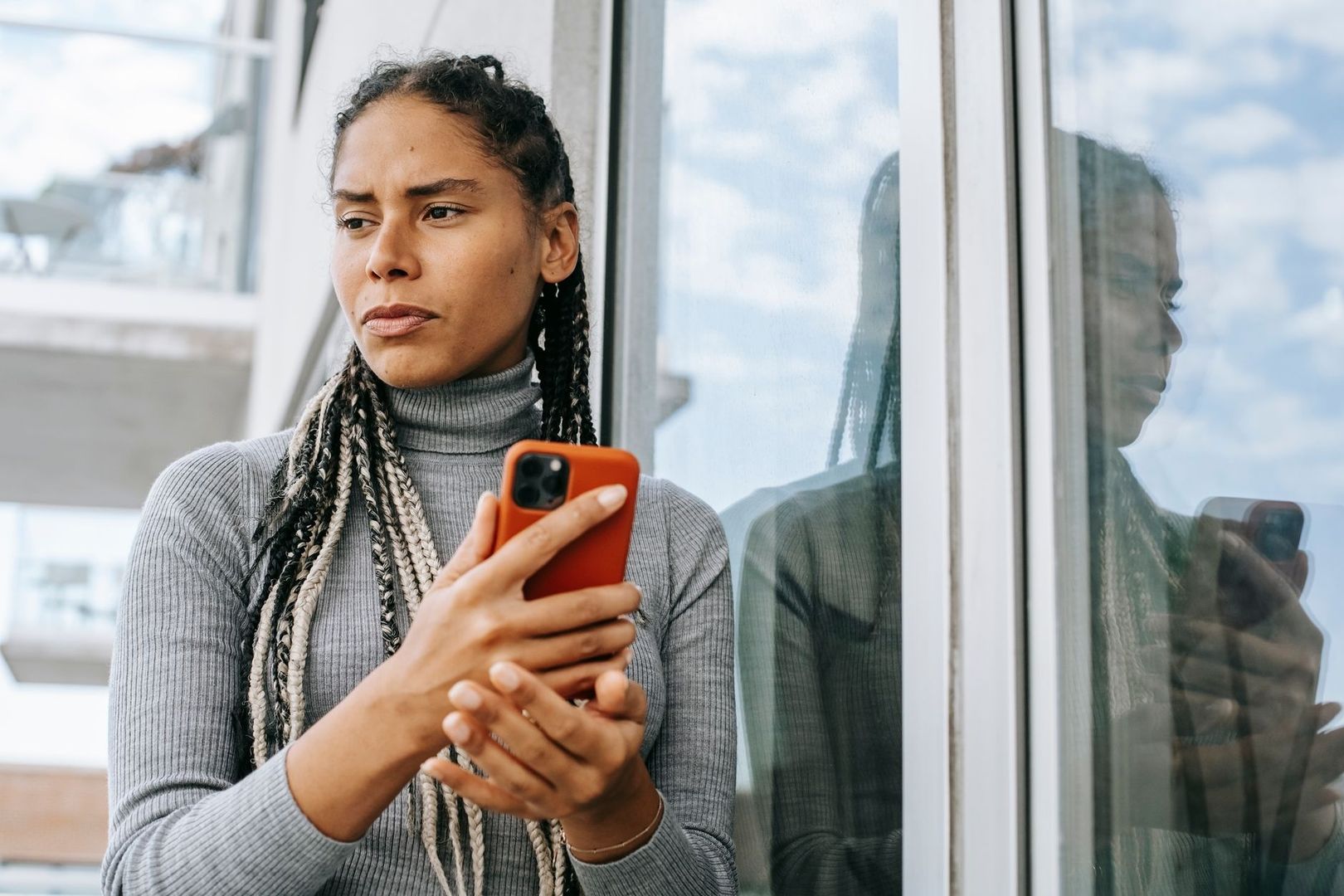 Vrouw kijkt bedachtzaam naar haar smartphone naast haar spiegelbeeld