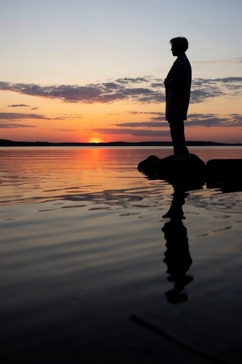 Silhouet van een peinzende persoon boven het water bij zonsondergang